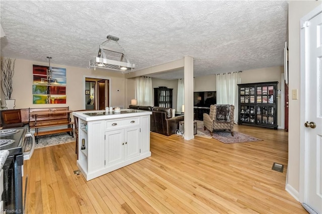 kitchen featuring visible vents, an island with sink, open floor plan, white cabinetry, and light wood finished floors