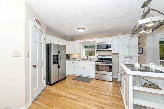 kitchen featuring light wood-type flooring, light countertops, appliances with stainless steel finishes, white cabinets, and a textured ceiling