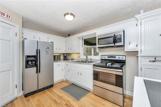 kitchen with a sink, stainless steel appliances, light wood-style flooring, and white cabinetry