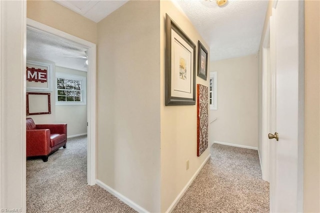 hallway with light carpet, a textured ceiling, and baseboards