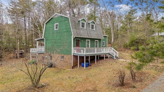 view of front facade featuring stairs, a gambrel roof, roof with shingles, and a wooden deck