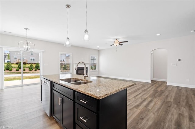 kitchen with light stone countertops, ceiling fan with notable chandelier, a kitchen island with sink, sink, and decorative light fixtures