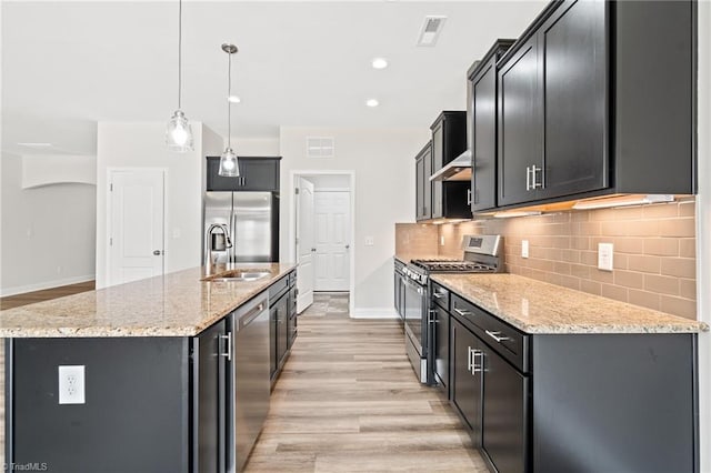 kitchen featuring sink, stainless steel appliances, light stone counters, pendant lighting, and a center island with sink