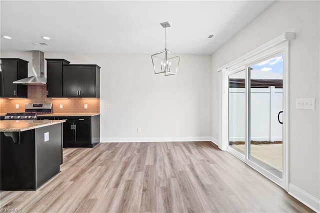 kitchen featuring a kitchen bar, wall chimney range hood, decorative light fixtures, an inviting chandelier, and stainless steel range oven