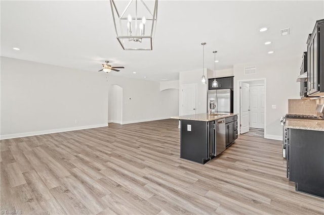 kitchen featuring a center island with sink, hanging light fixtures, ceiling fan, appliances with stainless steel finishes, and light stone counters