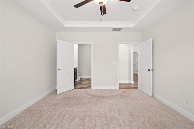 unfurnished bedroom featuring a raised ceiling, ceiling fan, crown molding, and carpet