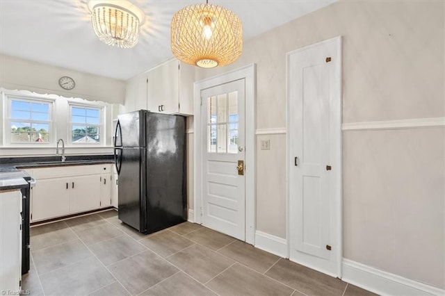 kitchen with sink, white cabinetry, black fridge, a chandelier, and pendant lighting