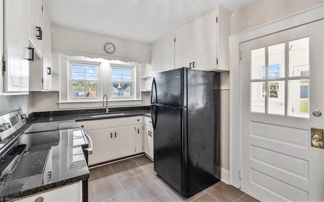 kitchen featuring sink, white cabinetry, black fridge, dark stone countertops, and light tile patterned floors