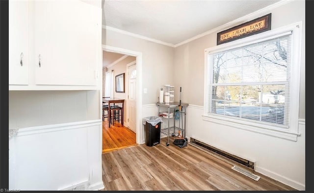 interior space with a wainscoted wall, visible vents, light wood-type flooring, and ornamental molding