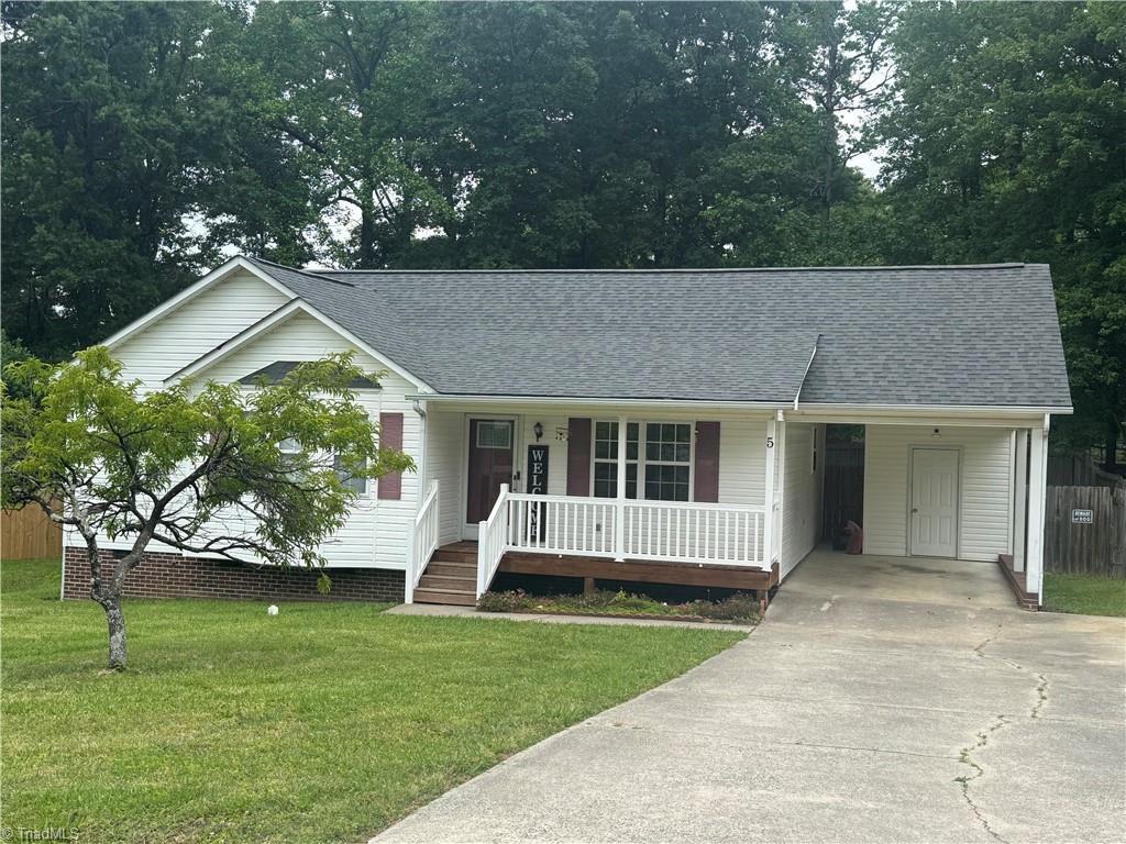 view of front of property featuring driveway, covered porch, a front lawn, roof with shingles, and a carport