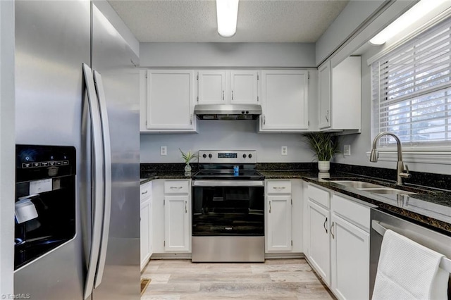 kitchen featuring appliances with stainless steel finishes, white cabinetry, dark stone countertops, and sink