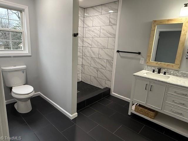 bathroom featuring a tile shower, tile patterned flooring, vanity, and toilet