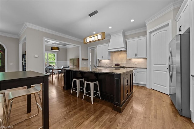 8441 Alice Player Dr, Oak Ridge, NC 27310 - kitchen featuring freestanding refrigerator, premium range hood, wood finished floors, white cabinetry, and ornamental molding