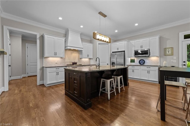 8441 Alice Player Dr, Oak Ridge, NC 27310 - kitchen featuring appliances with stainless steel finishes, premium range hood, a kitchen breakfast bar, white cabinetry, and recessed lighting