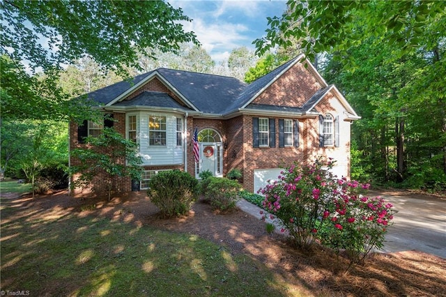 raised ranch featuring brick siding, an attached garage, and driveway