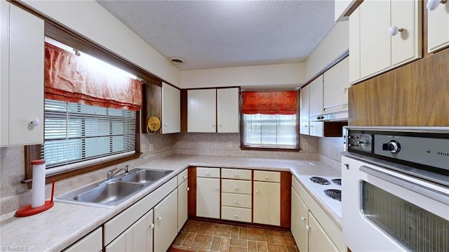 kitchen with light countertops, under cabinet range hood, a sink, and white appliances