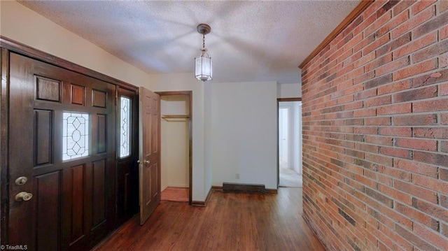 foyer with wood finished floors, a textured ceiling, baseboards, and brick wall
