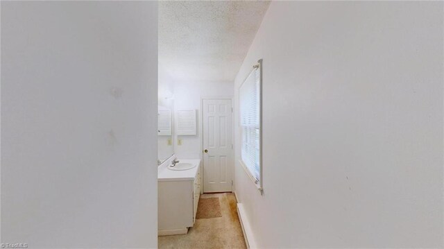 corridor featuring baseboards, a sink, and a textured ceiling
