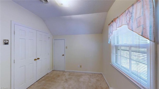 unfurnished bedroom featuring vaulted ceiling, a closet, baseboards, and light carpet