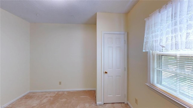 unfurnished bedroom featuring light carpet, a textured ceiling, and baseboards