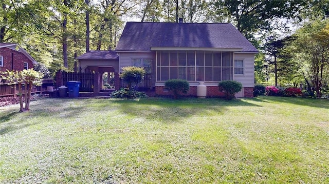 view of front of home with a sunroom, roof with shingles, and a front yard