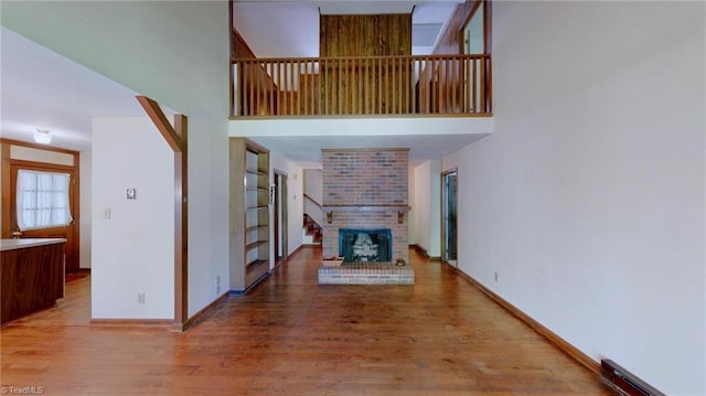 unfurnished living room featuring baseboards, a brick fireplace, wood finished floors, and a high ceiling