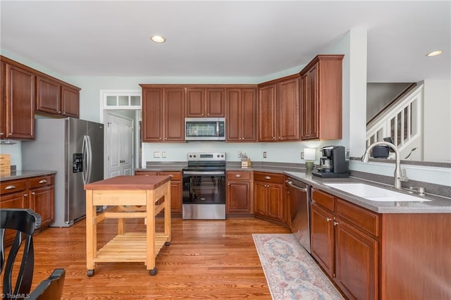 kitchen with appliances with stainless steel finishes, a sink, light wood finished floors, recessed lighting, and brown cabinets