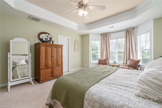 bedroom with a tray ceiling, baseboards, multiple windows, light colored carpet, and crown molding
