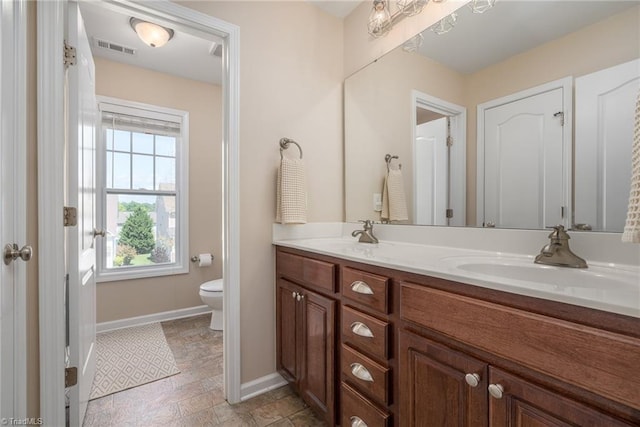 bathroom with baseboards, double vanity, toilet, and stone finish flooring