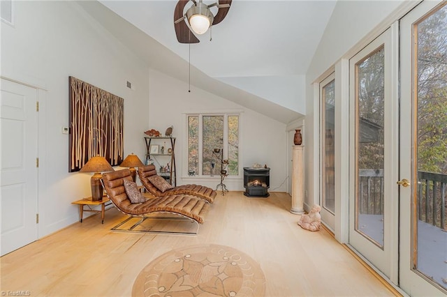 living area featuring decorative columns, vaulted ceiling, ceiling fan, hardwood / wood-style flooring, and a wood stove