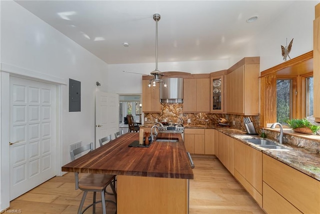 kitchen featuring light brown cabinetry, sink, a center island with sink, dark stone countertops, and light hardwood / wood-style floors