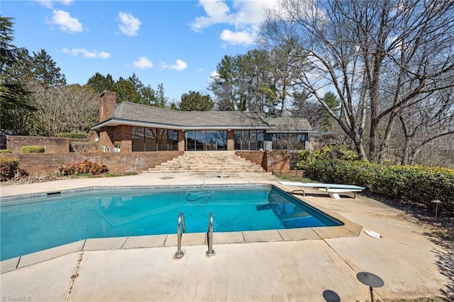 outdoor pool with a patio area, stairs, and a diving board