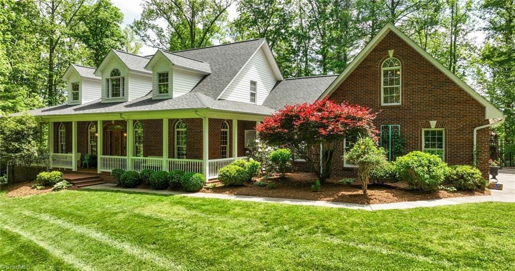 1670 Skyland Dr, Wilkesboro, NC 28697 - new england style home featuring covered porch, brick siding, roof with shingles, and a front lawn