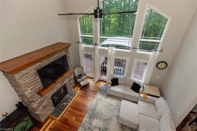 living room featuring ceiling fan, a high ceiling, a stone fireplace, and wood finished floors