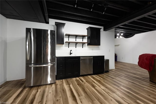 kitchen with light wood-type flooring, appliances with stainless steel finishes, dark cabinetry, and a sink