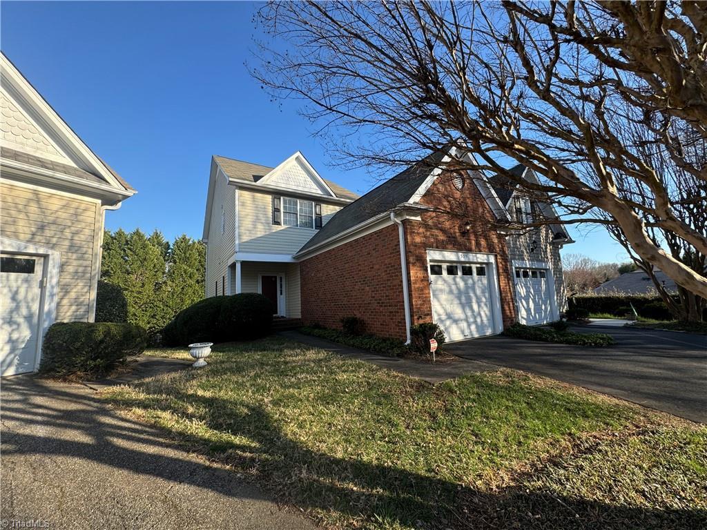 view of side of home featuring brick siding, a lawn, driveway, and a garage