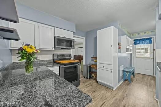 1630 Ploughboy Ln, Winston-Salem, NC 27103 - kitchen with stainless steel appliances, light wood-type flooring, white cabinetry, dark stone counters, and a textured ceiling