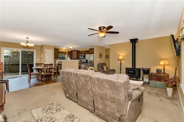 living room with ceiling fan with notable chandelier, light colored carpet, and a wood stove