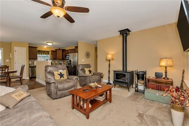 carpeted living room featuring ceiling fan and a wood stove