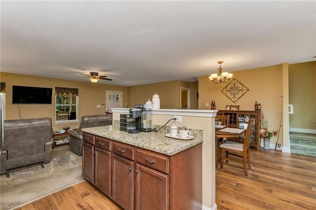 kitchen featuring pendant lighting, ceiling fan with notable chandelier, light stone countertops, and light hardwood / wood-style flooring