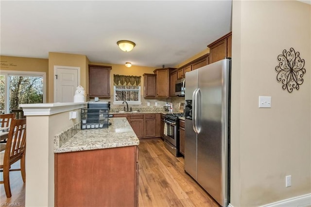 kitchen with sink, light hardwood / wood-style flooring, appliances with stainless steel finishes, tasteful backsplash, and light stone counters