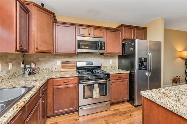 kitchen featuring light stone countertops, sink, stainless steel appliances, tasteful backsplash, and light hardwood / wood-style flooring