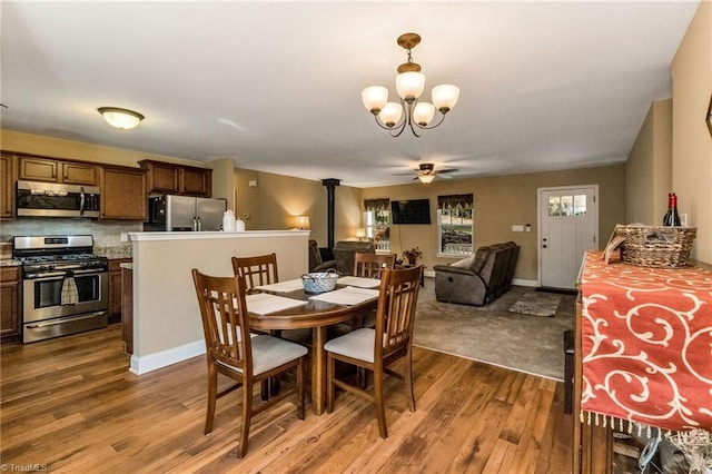 dining room featuring ceiling fan with notable chandelier, hardwood / wood-style flooring, and a wood stove