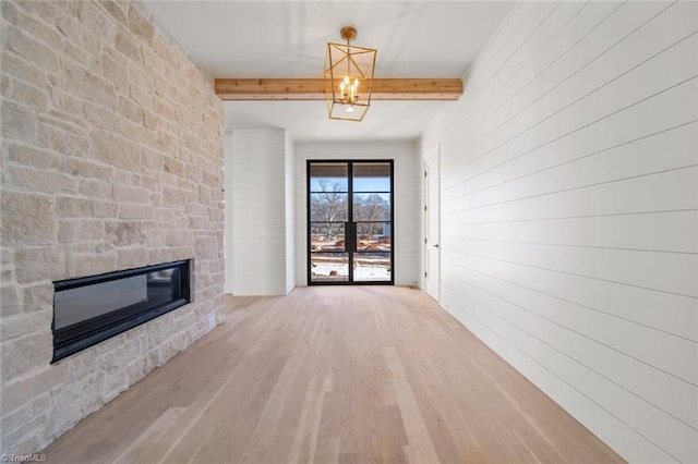 unfurnished living room featuring a chandelier, wood walls, hardwood / wood-style floors, beam ceiling, and a fireplace