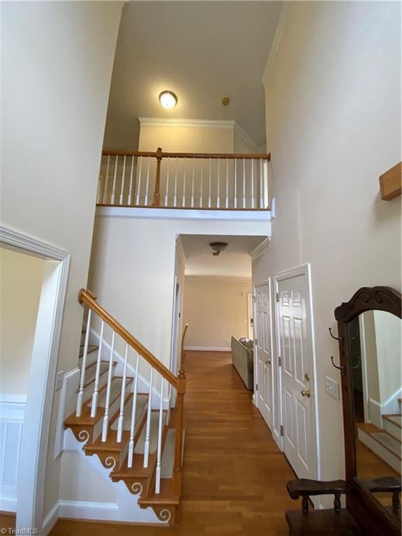 staircase with crown molding, a towering ceiling, and hardwood / wood-style flooring