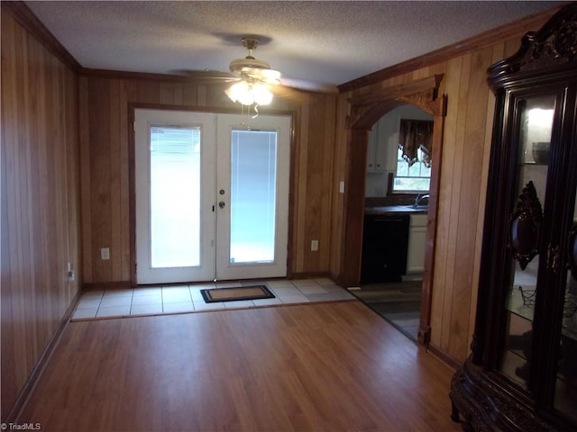 doorway with ceiling fan, a textured ceiling, wood walls, and light hardwood / wood-style floors