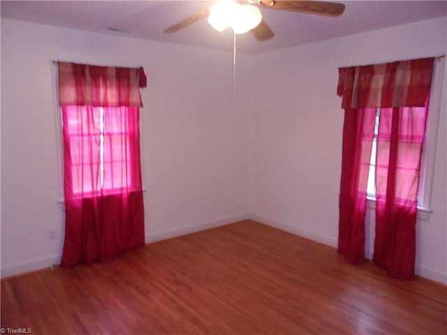 empty room with a healthy amount of sunlight, ceiling fan, and hardwood / wood-style flooring