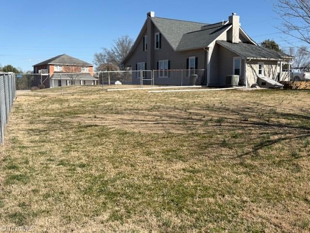 rear view of property featuring a yard, fence, a chimney, and central AC unit