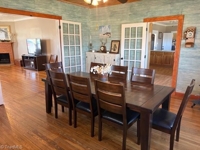 dining area with ceiling fan, a fireplace, crown molding, and wood finished floors