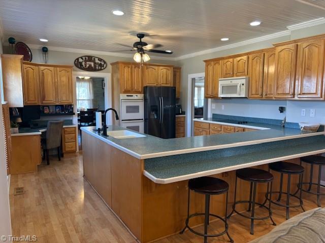 kitchen featuring light wood-style flooring, a peninsula, a sink, brown cabinets, and black appliances